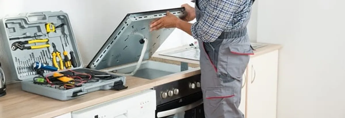 Cooktop repair technician lifting a built-in stovetop for service in Naperville, IL
